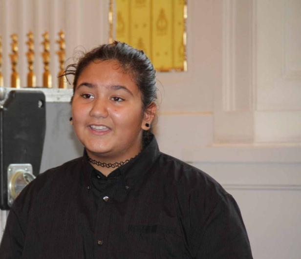 Ein junges Mädchen mit dunklem Haar und einem schwarzen Oberteil lächelt.