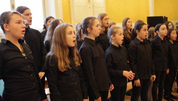 Eine Gruppe von Kindern in schwarzen Hemden singt in einem Chor.