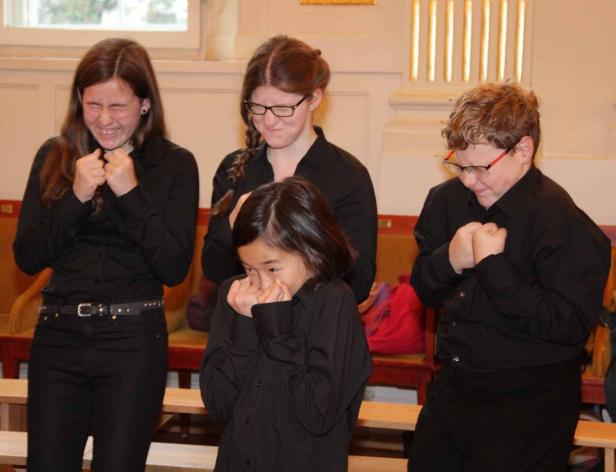 Vier Kinder in schwarzen Hemden scheinen sich vor Schmerzen zu krümmen.
