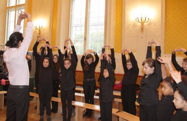 Eine Gruppe von Kindern macht mit einem Lehrer Dehnübungen in einem Raum.