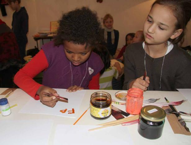 Zwei Mädchen bemalen mit Federn und Tinte Papierbögen.
