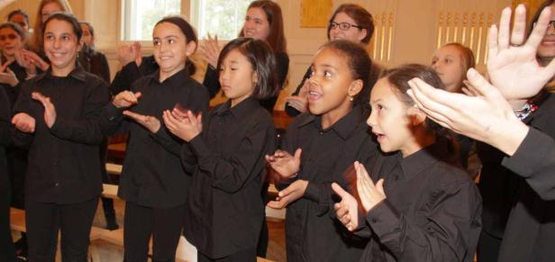 Ein Kinderchor in schwarzen Hemden singt und klatscht in die Hände.