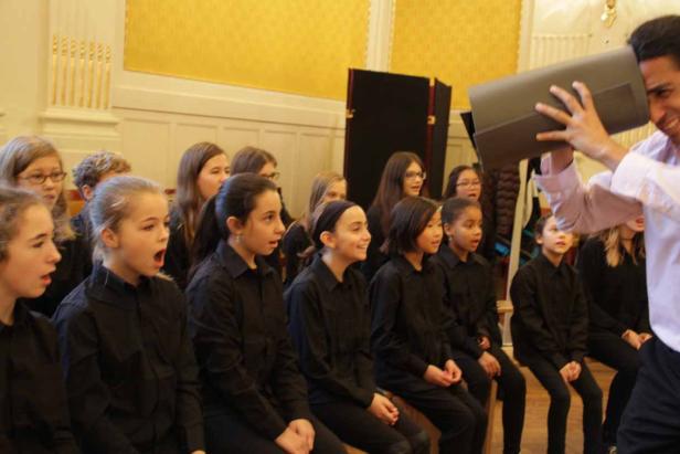 Ein Chor von Kindern und ein Dirigent mit einer Notenmappe.