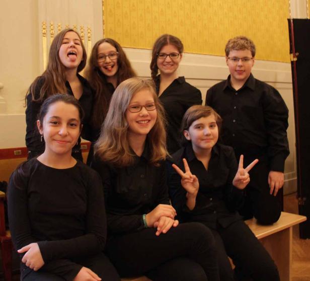 Eine Gruppe von sieben Jugendlichen posiert in schwarzen Hemden für ein Foto.