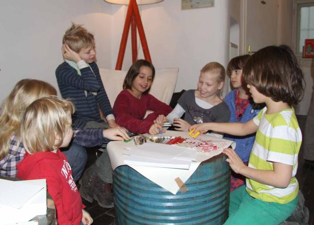 Eine Gruppe Kinder sitzt an einem Tisch und bastelt mit Stiften und Papier.