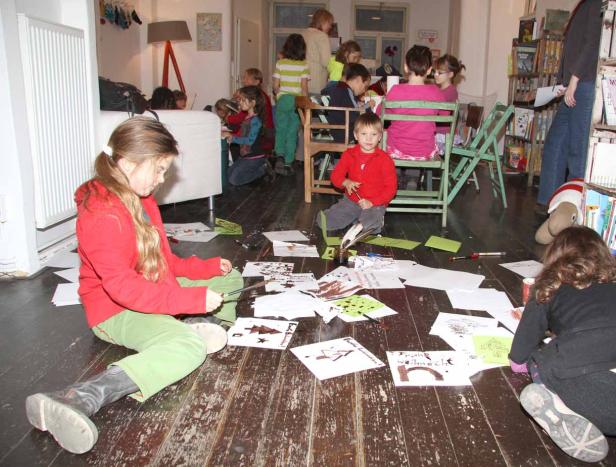 Kinder sitzen auf dem Boden und an Tischen und basteln Weihnachtskarten.