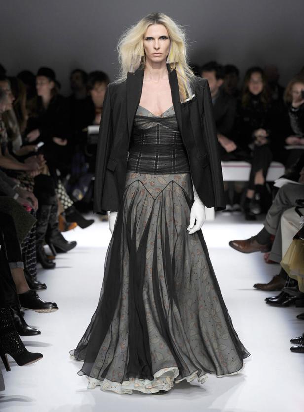 Eine Frau in einem langen Kleid und Blazer auf einem Laufsteg.