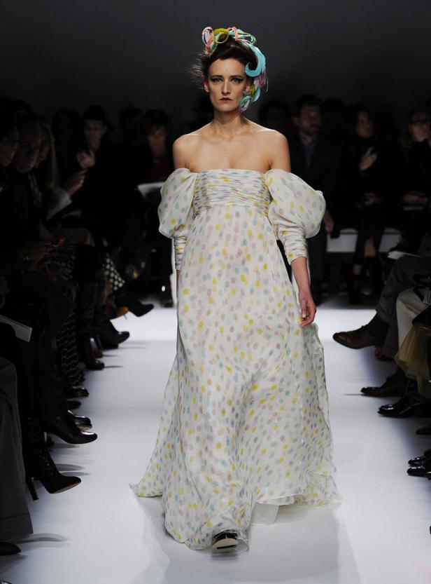 Ein Model präsentiert ein schulterfreies Kleid mit bunten Punkten auf dem Laufsteg.