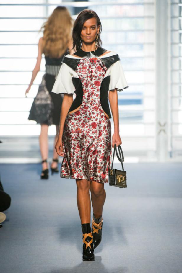 Eine Frau in einem gemusterten Kleid mit Blumenmuster und schwarzen Stiefeln auf einem Laufsteg.