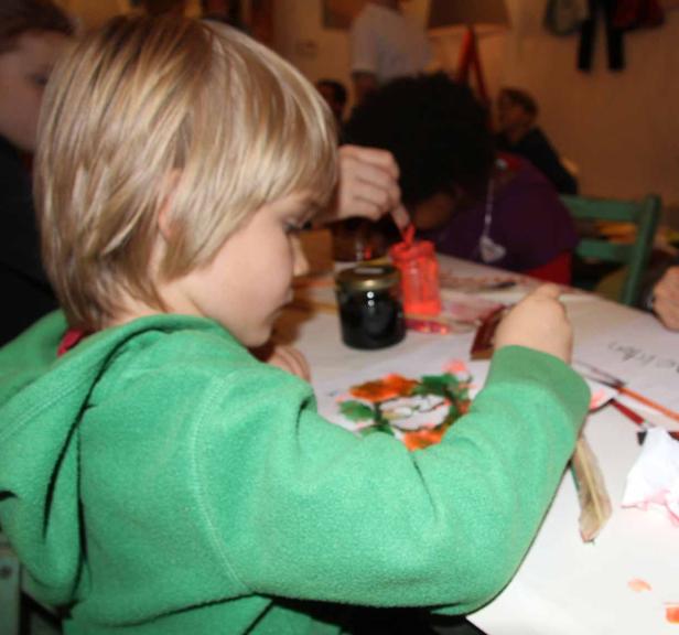 Ein Junge mit blonden Haaren malt mit Farben auf einem Blatt Papier.