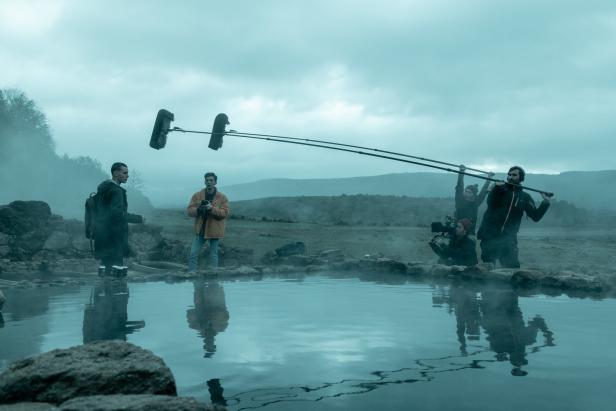 Ein Filmteam dreht eine Szene an einem See mit Nebel und Bergen im Hintergrund.