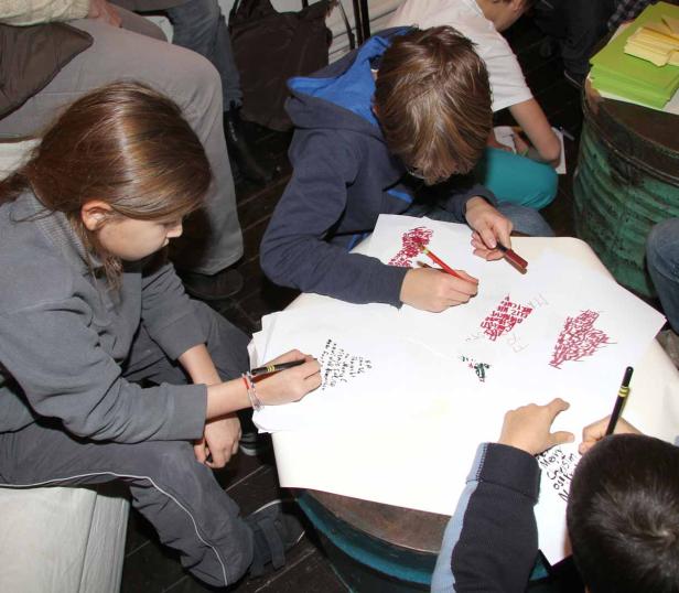Kinder sitzen an einem Tisch und schreiben oder malen auf Papier.