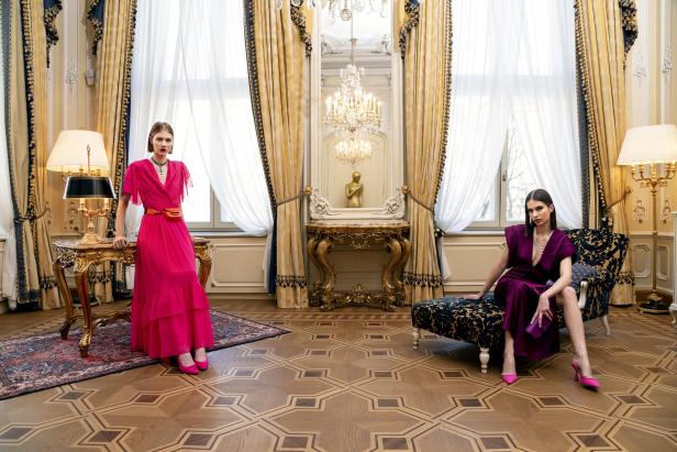Zwei Frauen posieren in eleganten Kleidern in einem prunkvollen Raum.