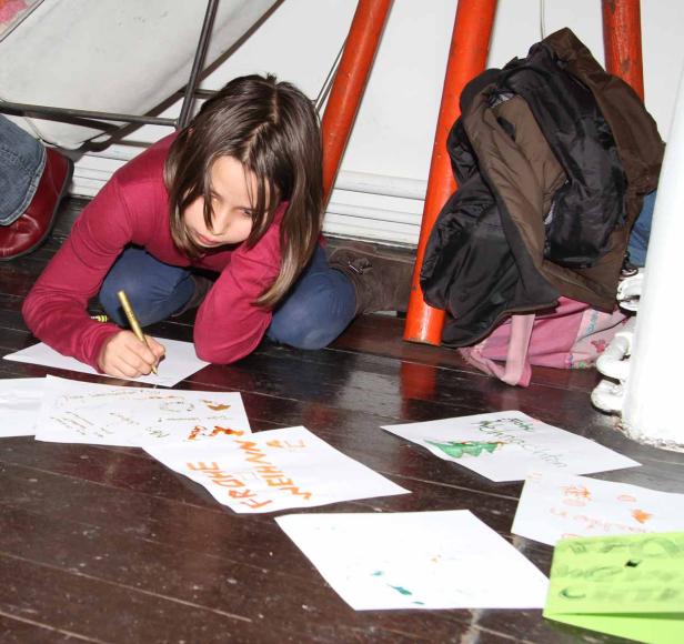 Ein Mädchen kniet auf dem Boden und schreibt Weihnachtskarten.