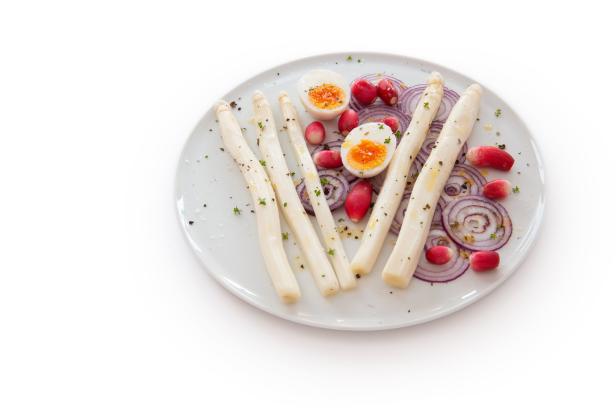 Ein Teller mit weißem Spargel, Radieschen, roten Zwiebeln und halbierten Eiern.