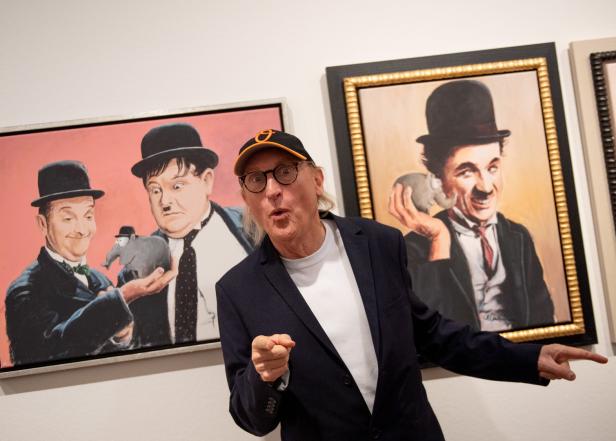 Ein Mann posiert vor Gemälden von Charlie Chaplin sowie Laurel und Hardy.