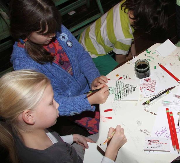 Drei Kinder sitzen an einem Tisch und schreiben Weihnachtskarten.