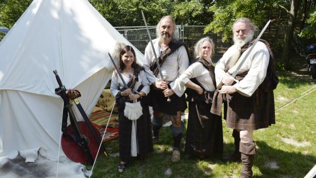 Eine Gruppe von Personen in schottischer Tracht posiert mit Schwertern vor einem Zelt.