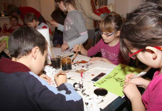 Kinder sitzen an einem Tisch und basteln mit Farbe und Federn Weihnachtskarten.