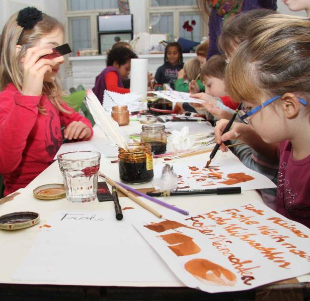 Kinder sitzen an einem Tisch und schreiben mit Tinte Weihnachtskarten.