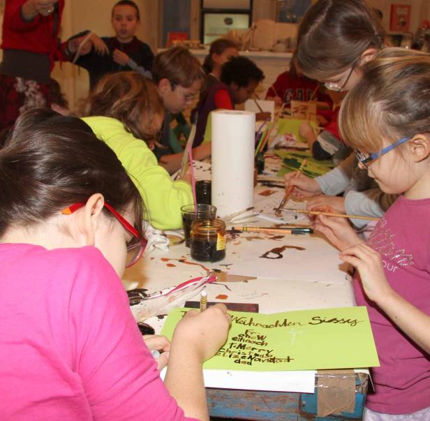 Kinder sitzen an einem Tisch und malen Weihnachtskarten.