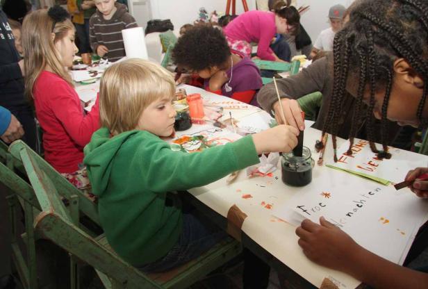 Kinder sitzen an einem Tisch und bemalen Weihnachtskarten.