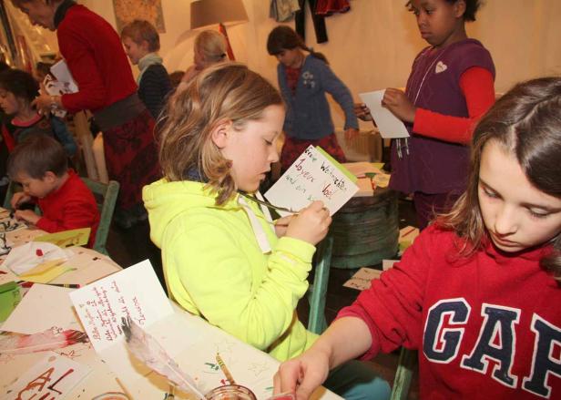 Kinder schreiben und basteln Weihnachtskarten an Tischen.