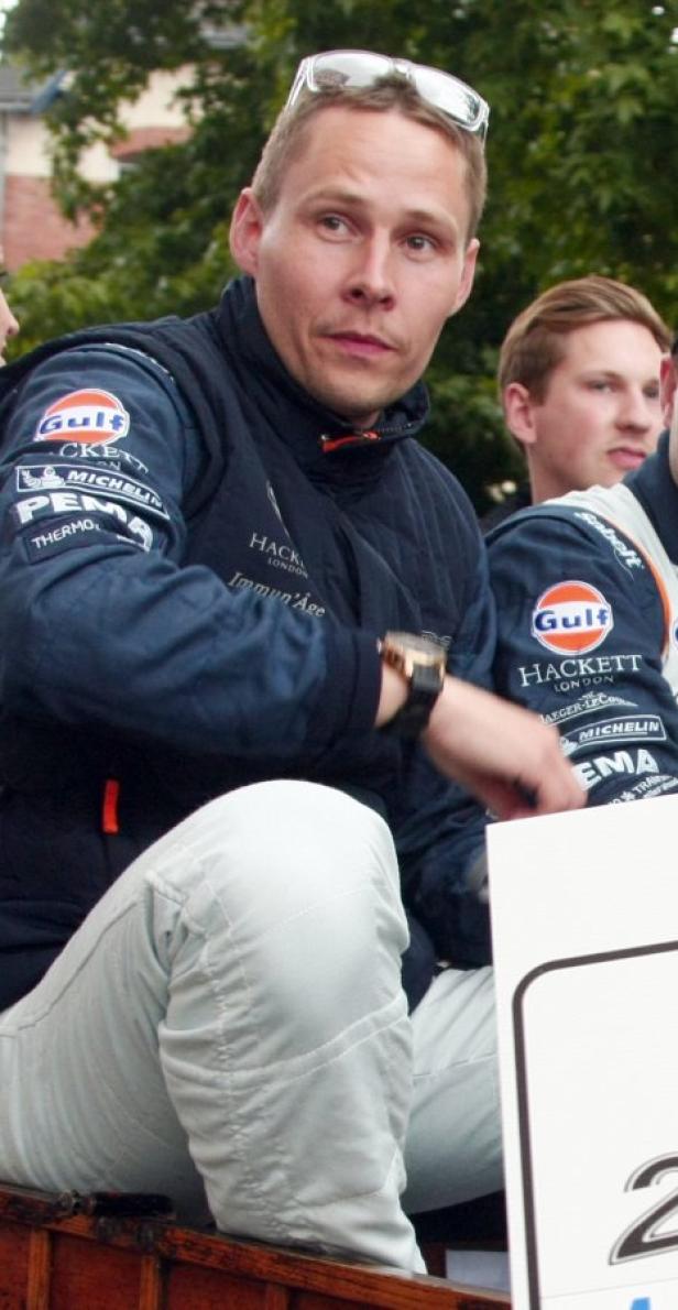 Ein Mann mit Sonnenbrille auf dem Kopf, bekleidet mit einer Jacke mit Sponsorenlogos.