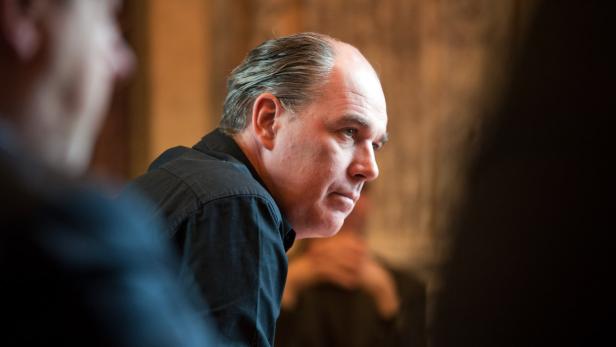 Ein Mann mit schwarzem Hemd schaut aufmerksam zur Seite.