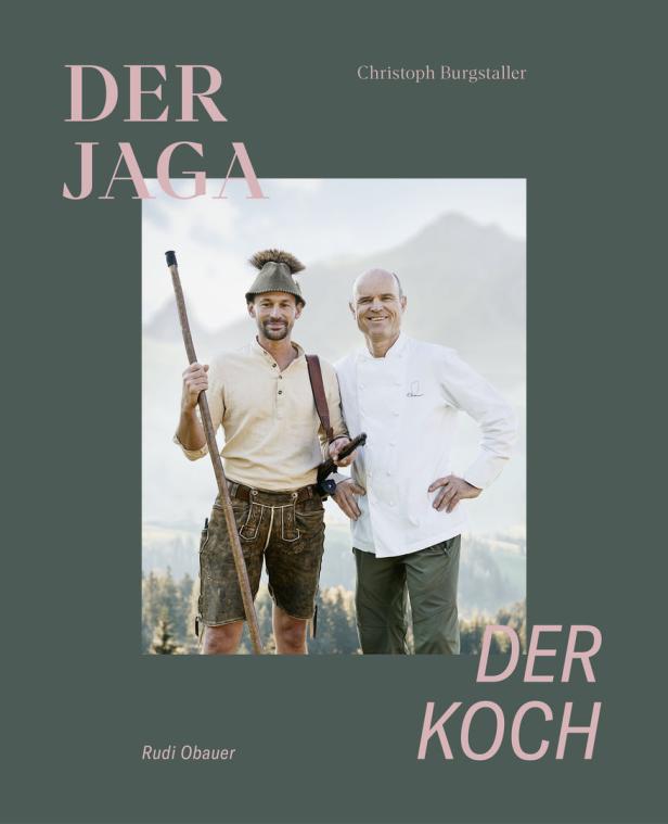 Ein Jäger in Tracht und ein Koch stehen vor einer Bergkulisse.