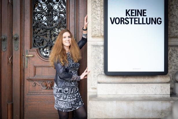 Eine Frau posiert neben einer Holztür und einer Werbetafel mit der Aufschrift „Keine Vorstellung“.