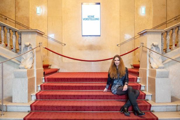 Eine Frau sitzt auf einer mit rotem Teppich belegten Treppe vor einem Schild mit der Aufschrift „Keine Vorstellung“.