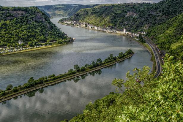 Blick auf den Rhein mit einer kleinen Insel und bewaldeten Hügeln.
