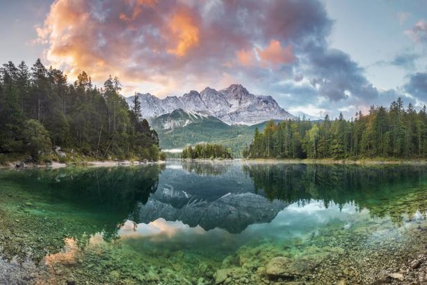 Der Eibsee spiegelt die Zugspitze und den bewaldeten Uferbereich wider.