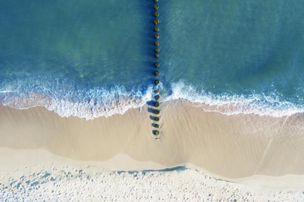 Luftaufnahme eines Strandes mit einer Reihe von Holzpfählen im Wasser.
