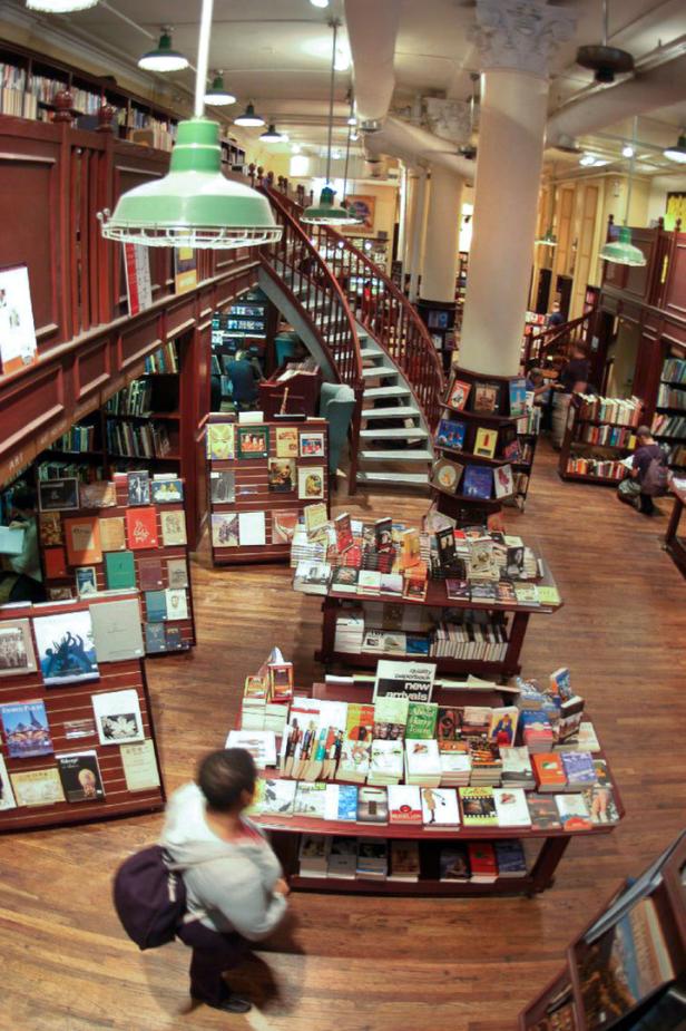 Blick in einen Buchladen mit Wendeltreppe und Tischen voller Bücher.