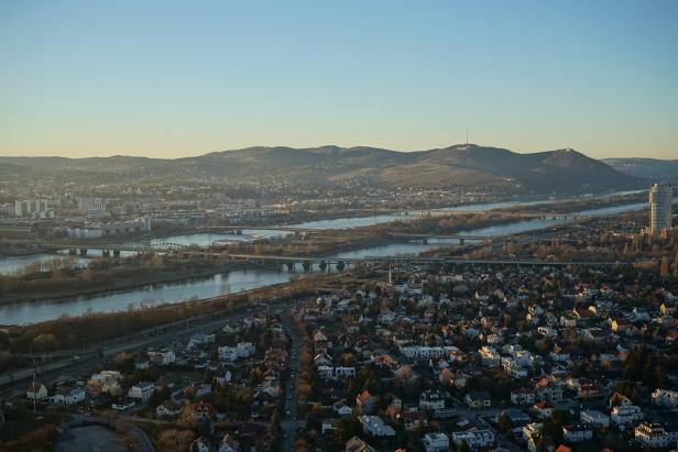 Luftaufnahme von Wien mit der Donau und dem Kahlenberg im Hintergrund.