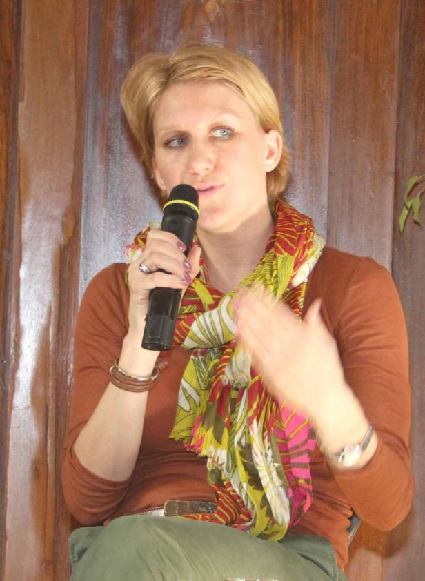 Eine Frau mit blonden Haaren spricht in ein Mikrofon und gestikuliert.