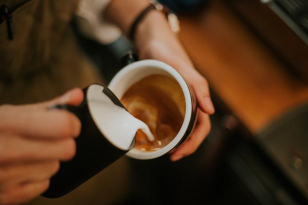Jemand gießt Milch in eine Tasse Kaffee.