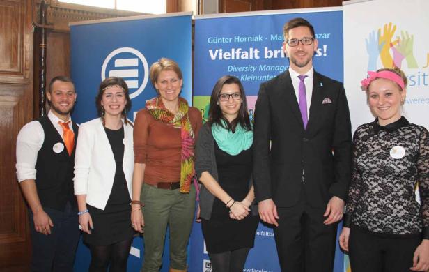 Eine Gruppe von sechs Personen posiert vor Bannern zum Thema Vielfalt.