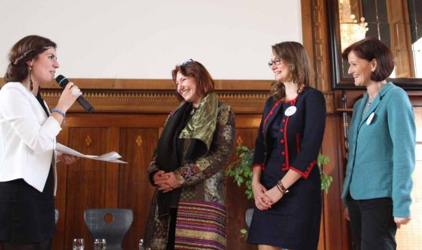 Eine Frau spricht bei einer Veranstaltung vor drei anderen Frauen in einem Raum mit Holzvertäfelung.