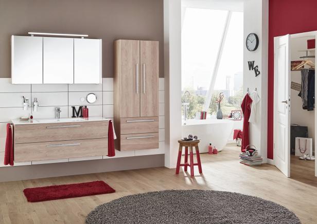 Ein modernes Badezimmer mit hellen Holzmöbeln, einer Badewanne und roten Akzenten.