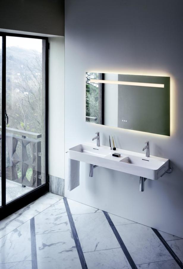 Ein modernes Badezimmer mit Doppelwaschbecken, beleuchtetem Spiegel und Marmorboden.