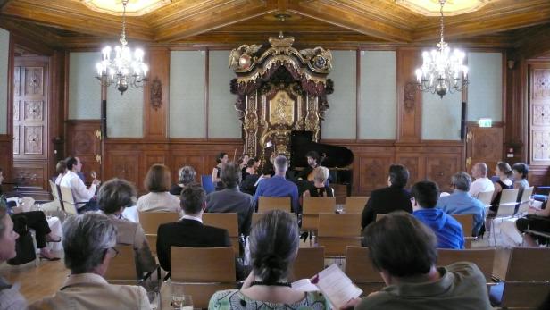 Zuschauer sitzen in einem Saal und lauschen einem klassischen Konzert.