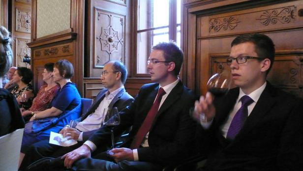 Gäste sitzen bei einer Veranstaltung mit Weingläsern in einem holzvertäfelten Raum.