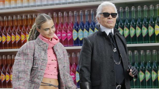 Cara Delevingne und Karl Lagerfeld posieren vor einem Regal mit bunten Getränkeflaschen.