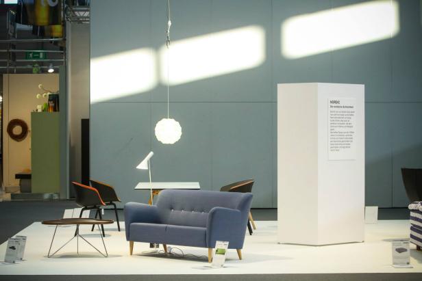Ein blaues Sofa steht auf einer Ausstellungsfläche mit weiteren Möbeln.