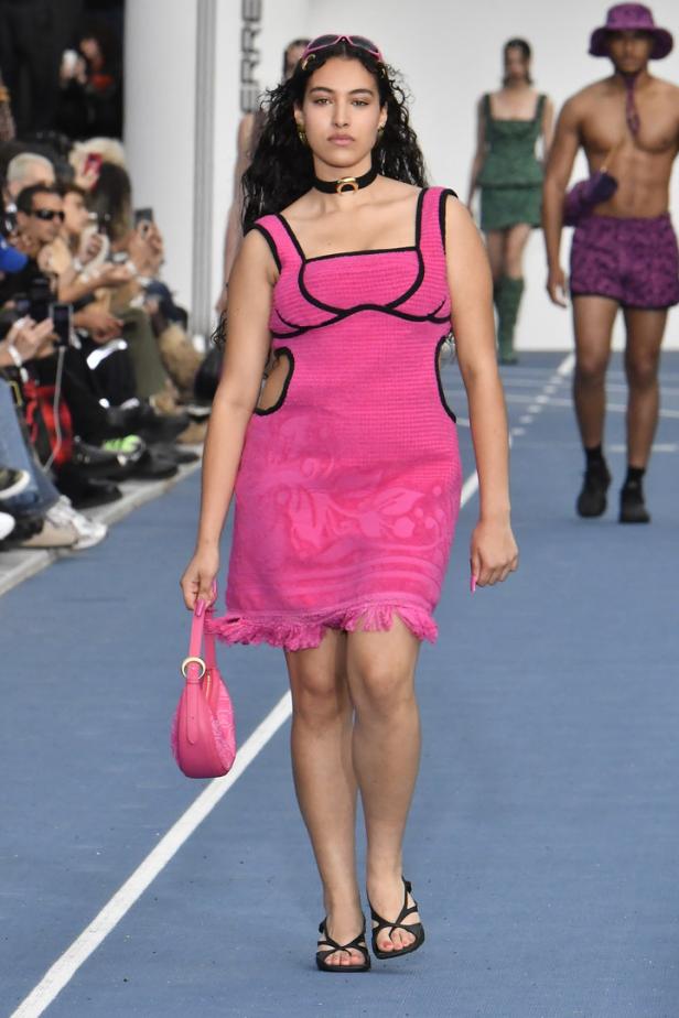 Eine Frau in einem pinkfarbenen Kleid mit passender Handtasche auf einem Laufsteg.