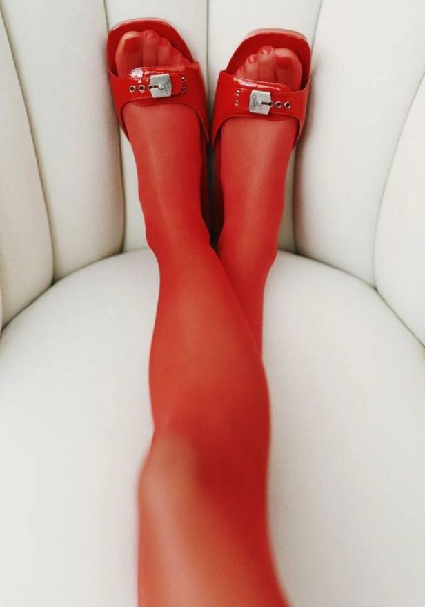 Beine mit roten Strumpfhosen und roten Sandalen auf einem weißen Sessel.