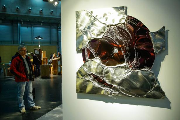 Ein Mann betrachtet ein abstraktes Metallkunstwerk an einer Wand.